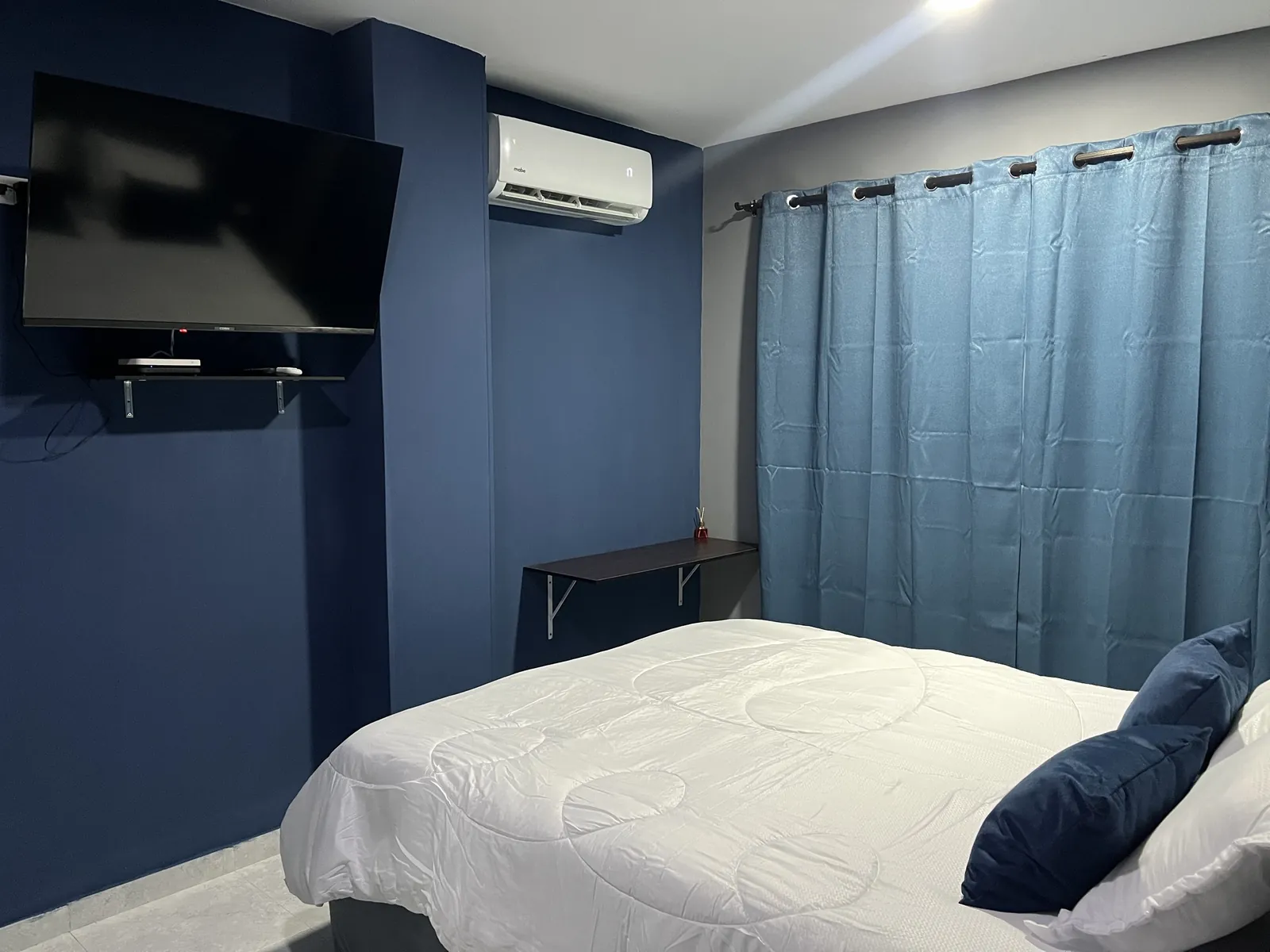 Habitación doble del Hotel Stay Villa Marta con paredes azules, cama doble, TV, aire acondicionado y cortina azul
